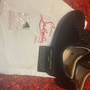 Svarta sneakers med nitar från Christian Louboutin - Säljer ett par svarta sneakers från Christian Louboutin med ikoniska röda sulor och svarta nitar på tån. Skorna har snörning och är tillverkade i skinn. Kommer med originalpåse och extra skosnören.