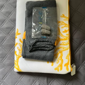 Vit och gul kuvertväska med dragkedja + sockor och öronproppar  - Säljer en stilren kuvertväska i vitt tyg med gult korallmönster och gul dragkedja. Väskan är rektangulär och har ett fräscht, somrigt uttryck. Perfekt för att bära småsaker eller använda som necessär. Materialet känns som bomull och väskan. Du får också med ett par sockor och ett per öronproppar 👍