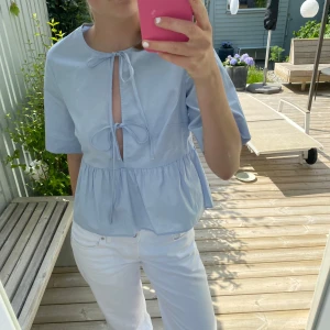 Ljusblå blus med knyt  - Supersöt ljusblå blus från H&M med volang nertill och två knyt framtill. Blusen har korta ärmar och en luftig, lite loose passform. Perfekt nu för sommaren. Använd fåtal gånger så väldigt fint skick.