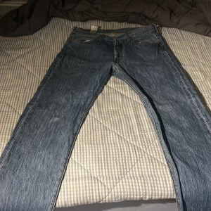 Levi's 501 blå jeans W32 L30 - Klassiska Levi's 501 jeans i blå denim med raka ben och normal passform. Byxorna har fem fickor, knappgylf och den ikoniska läderpatchen bak i midjan. Perfekta för dig som gillar tidlös stil och vill ha ett par slitstarka jeans.
