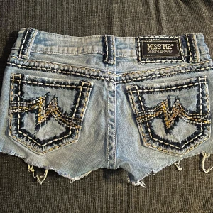Miss Me ljusblå jeansshorts med brodyr - Snygga ljusblå Lågmidjade jeansshorts från Miss Me med råa kanter och slitna detaljer. Shortsen har dekorativa broderier i svart och beige på fickorna samt kontrastsömmar runtom. Klassisk femficksmodell med knapp och dragkedja framtill. Lite sönder vid skrevet men ingen som syns på och enkelt att laga🤗