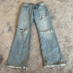 Ljusblå raka jeans från Zara - Ljusblå jeans från Zara med raka ben, slitna detaljer vid knä och benslut samt klassisk femficksmodell. Jeansen har hög midja och råa kanter nertill för en cool, avslappnad vibe. Perfekta för dig som gillar en trendig och avslappnad look.