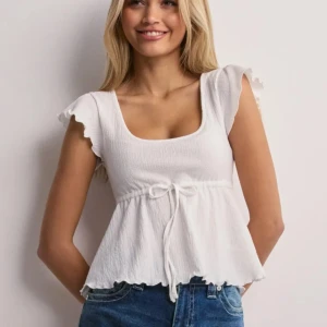 Vit blus med volangärm  - Supersöt vit blus med fyrkantig ringning, volangärmar och knyt i midjan. Perfekt till jeans eller kjol. Funkar att styla på många olika sätt och perfekt till en sommar outfit. Använd 1 gång