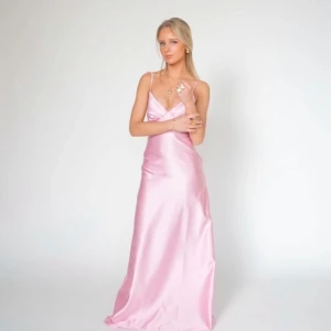 Ljusrosa Balklänning i satin Bystina - Supersnygg ljusrosa långklänning med smala axelband och v-ringning. Klänningen har en elegant, figurnära passform och är gjord i glansigt satinmaterial som ger en lyxig känsla. Perfekt för bal eller student! 💖 Jag har även sytt upp klänningen, så den passar mig som är 165cm. Nypris 1495 kr💕