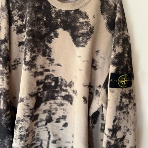 Stone Island beige sweatshirt L - Säljer en beige sweatshirt från Stone Island i storlek L med svart mönster över hela tröjan. Klassisk rund halsringning och ikonisk patch på ärmen. Perfekt för dig som gillar streetwear och vill sticka ut med en unik look.