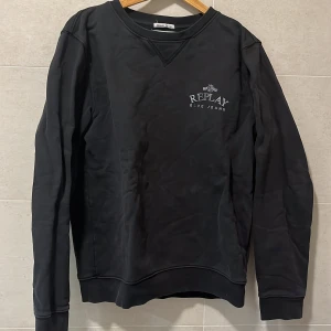 Svart sweatshirt från Replay L - Svart sweatshirt från Replay med tryckt logga på bröstet. Klassisk rund halsringning och långa ärmar. Tröjan är i mjuk bomull och har ribbade muddar vid ärmslut och nederkant. Perfekt för en chill och stilren look.
