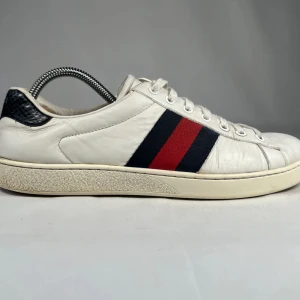 Gucci ace skor  vita sneakers med röd/blå rand - Snygga vita sneakers från Gucci i skinn med klassiska röd och marinblå ränder på sidan. Skon har rund tå, snörning och en detalj i svart ormskinnsmönster på hälen. Perfekt för dig som vill ha en clean men ändå lyxig look. 100% äkta. Pris pga ingen dust bag eller og box