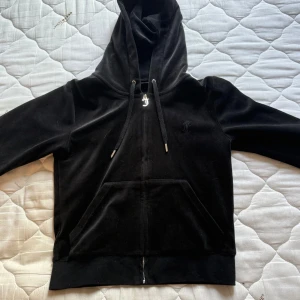 Svart velourkofta , Juicy Couture S - Svart velourkofta från Juicy Couture med huva, dragkedja och snörning. Klassisk hoodie-stil med känguruficka framtill och diskret JC-logga på bröstet. Knappast använd då den sitter lite tajt på mig. Matchande byxor säljs även till om det önskas självklart ingår paket pris isåfall (800kr)