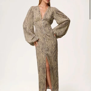 Zebramönstrad långklänning från Adoore - Intressekoll! Supersnygg långklänning från Adoore med zebramönster i beige och grått. Klänningen har djup v-ringning, långa puffärmar och knappar hela vägen framtill samt en slits. Storlek 40, helt oanvänd med prislapp!