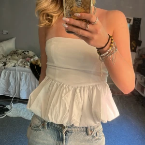 Vit bandå topp  - Supersöt vit bandeau topp från FP Sister med volang nertill och smockad rygg. Toppens axelbandslösa design ger en clean och fräsch look, perfekt till jeans eller kjol. Materialet känns lätt och luftigt, vilket gör den nice för varma dagar.