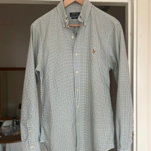 Rutig skjorta Polo Ralph Lauren slim fit - Snygg rutig skjorta från Polo Ralph Lauren i slim fit-modell. Skjortan är vit med gröna och blå rutor, har klassisk krage, knappar framtill och broderad logga på bröstet. Perfekt för dig som gillar stilrena och tidlösa plagg. Sjukt fräsch inför sommaren! 