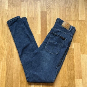 Dam Nudie Jeans Hightop Tilde Blå Jeans - Nudie Jeans i modellen Hightop Tilde och färgen Blå till Dam. OBS! Sömnen på vänsterben, yttersida, håller på att gå upp! Fixas lätt till av någon bra med nål! Storlek: 32 W, 32 L, Midja: 37.5 cm Ytterben: 112 cm Benöppning: 13.5 cm Material: 92% Organic Cotton, 6% Polyester, 2% Elastane.