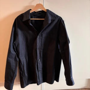 Mörkblå overshirt från Zara - Stilren mörkblå overshirt från Zara i bomull. Klassisk krage, knäppning framtill och en bröstficka. Långärmad modell med enkel och clean look.