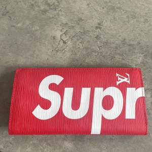Supreme x Louis Vuitton röd plånbok - Riktigt fet röd plånbok från Supreme x Louis Vuitton med stort vitt Supreme-tryck. Gjord i exklusivt präglat skinn med flera kortfack och plats för sedlar. Insidan har initialerna E.F. präglade i vitt. Perfekt för dig som vill sticka ut med en ikonisk accessoar. Varan är knappast använd där min mamma har använt den max 5 gånger. PRISET ÄR INTE HUGGET I STEN SÅ KOM MED FRÅGOR ‼️ LOWBALLA SÖNDER MIG