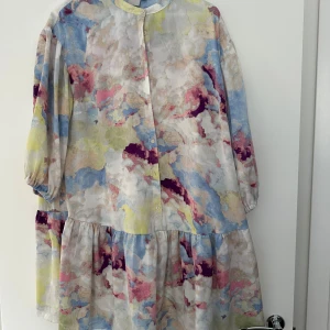 Färgglad kortklänning från ICHI - Superfin kortklänning från ICHI med ett unikt, abstrakt mönster i pastelliga toner av blått, rosa, gult och vitt. Klänningen har knappar framtill, volang nedtill och trekvartsärmar med lätt puff. Perfekt för dig som gillar färg och en luftig, loose passform.