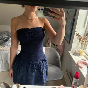 Marinblå kort klänning med volang - Supersöt, marinblå, kort axelbandslös klänning med smockad överdel och volangig nederdel. Superfint skick!