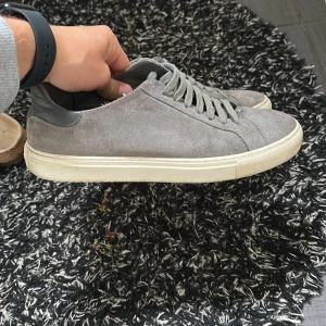 Grå mockasneakers från Axel Arigato - Snygga sneakers i grå mocka från Axel Arigato med ljusgrå snörning och vit platt sula. Box och allting medföljer. 