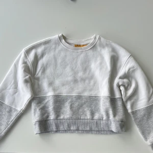 Vit och grå croppad sweatshirt - Snygg croppad sweatshirt i vitt och ljusgrått från Gina tricot. Den är i fint skick, använd fåtal gånger. Storlek 146/152 men passar XXS.