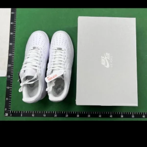 Nike Air Force 1 helvita sneakers - Klassiska Nike Air Force 1 sneakers i helvitt skinn med perforerad tå, rund tå och platt sula. Snygg och tidlös modell med snörning och diskret Nike-logga på sidan. Perfekta för dig som gillar clean och stilren streetwear.