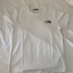 Vit t-shirt från The North Face - Vit t-shirt från The North Face med klassisk logga på bröstet. Enkel och stilren design med rund hals och korta ärmar. Perfekt för dig som gillar cleana basplagg och streetwear vibes. storlek 146/152
