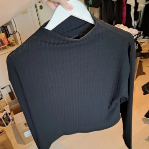 Svart ribbad croppad tröja Gina Tricot - Svart långärmad croppad tröja från Gina Tricot. Tröjan är ribbad och har en enkel, stilren design med rund hals. Perfekt att matcha med höga jeans eller kjol för en clean look.