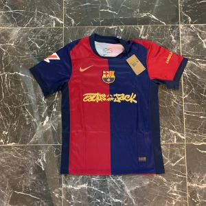 FC Barcelona Lamine Yamal tröja Nike S - FC Barcelona matchtröja från Nike i storlek S med Lamine Yamal och nummer 19 på ryggen. Tröjan är röd och blå med klubbmärke, Nike-logga och gul text. Korta ärmar och tillverkad i lätt funktionsmaterial, perfekt för fotboll eller supporterliv.