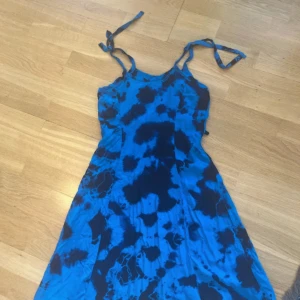 Blå batikmönstrad sommarklänning - Supersnygg blå klänning med batikmönster och knytbara axelband. Lätt och flowy modell som passar perfekt för varma dagar. Klänningen har en kort längd och är ärmlös, vilket ger en chill och avslappnad vibe.
