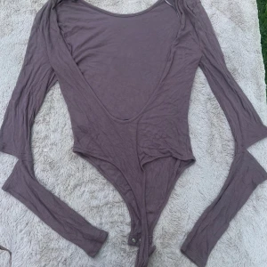 Ljuslila ribbad body från Rebecca Stella - Supersnygg ljuslila body från Rebecca Stella i ribbad bomullsmix. Djup urringning i ryggen, öppen i ryggen  långa ärmar och tryckknappar i grenen. Perfekt att styla med jeans eller kjol för en trendig look.