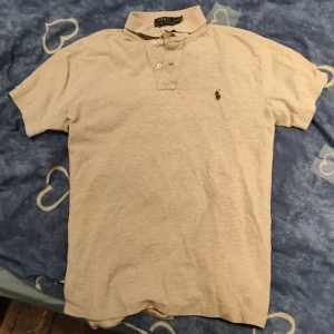 Beige pikétröja från Polo Ralph Lauren - Klassisk beige pikétröja från Polo Ralph Lauren med korta ärmar och krage. Tröjan har knäppning med tre knappar och den ikoniska broderade loggan på bröstet. Perfekt för en clean och stilren look. pris kan diskuteras och jag kan lova att tröjan är helt äkta