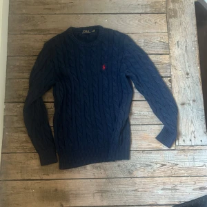 Mörkblå stickad tröja Polo Ralph Lauren - Kabelstickad mörkblå tröja från Polo Ralph Lauren. Sorry för att bilderna e dåliga inte min starka sida, fråga om fler bilder. Men annars är den knappt använd och i fint skick. Priser är inte hugget i sten och hör av er vid intresse