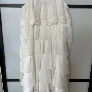 Vit volangklänning med spetsdetaljer - Superfin vit långklänning med flera lager volanger och spetsdetaljer upptill. Klänningen har tunna axelband, diskret prickigt mönster och dragkedja i ryggen. Perfekt för sommaren🥰