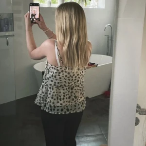 Beige prickig volang-linnetopp - Supersöt beige linnetopp med svarta prickar och volangdetaljer. Tunt, luftigt material med smala axelband och dragkedja i sidan. Perfekt för varma dagar när du vill ha en chill och trendig look.