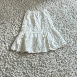 Vit volangkjol från Lindex Kids - Supersöt vit kjol från Lindex Kids med broderade hålmönster och volang nertill. Kjolen har resår i midjan för skön passform och är gjord i mjuk bomull. Perfekt för sommarens alla äventyr!