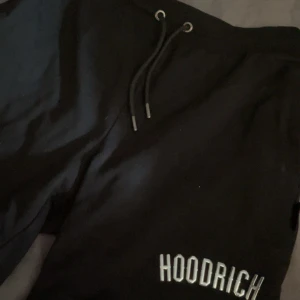 Svarta Hoodrich shorts  - Svarta mjukisshorts från Hoodrich i storlek S. Byxorna har snörning i midjan och Hoodrich-logga broderad på benet samt en metallbricka med loggan. Perfekta för chill eller streetwear-stil.