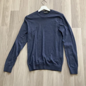 Blå merinoulltröja från Dressmann - Mörkblå långärmad tröja från Dressmann i mjuk merinoull. Enkel och stilren design med rund halsringning och ribbade muddar vid ärmslut och nederkant. Perfekt för lager-på-lager och funkar året runt.