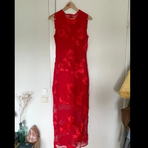 Röd blommig långklänning från YAS - Superfin röd långklänning från YAS med broderade blommor och transparent meshdetaljer. Ärmlös modell med rund halsringning och dragkedja samt knappar i ryggen. Perfekt för dig som vill sticka ut med en elegant look! (Aldrig använd, endast provad!)