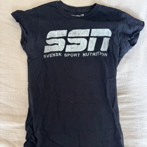 Svart SSN t-shirt med tryck - Svart t-shirt från SSN Svensk Sport Nutrition i bomull med stort vitt logotryck på bröstet. Klassisk rund hals och korta ärmar. Perfekt för dig som gillar sportig och enkel stil.