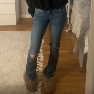 Blå bootcut jeans med slitna knän - Säljer ett par blå jeans som är bootcut och med två snygga hål som jag klippt själv vid knäna. Tyvärr för små för mig så därför säljer jag. Bilderna blev inte så bra så skriv om ni vill ha bättre bilder☺️