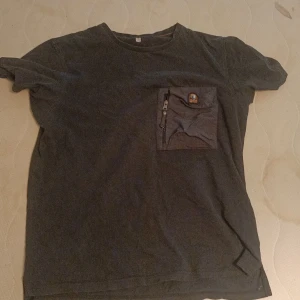 Svart t-shirt från Parajumpers S - Svart t-shirt från Parajumpers i bomull med en stor, cool bröstficka i nylonmaterial och dragkedja. Klassisk passform och rund halsringning. Perfekt för dig som gillar streetwear med funktionella detaljer. Äkta är den, skann funkar även