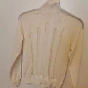 Vit polotröja med håldetaljer - Vit polotröja med unika håldetaljer på framsidan som ger en cool och edgy look. Tröjan är ribbstickad i halsen och har långa ärmar samt muddar vid ärmslut och nederkant. Materialet är en mix av bomull och polyester för en mjuk känsla. Från H&M