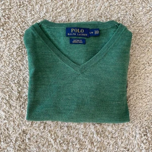 Grön merinoullströja Polo Ralph Lauren - Snygg grön tröja från Polo Ralph Lauren i mjuk merinoull. V-ringad modell med lång ärm och klassisk broderad logga på bröstet. Perfekt för dig som gillar stilrena och bekväma plagg med premiumkänsla.