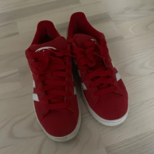 Röda Adidas Campus sneakers i mocka - Snygga röda Adidas Campus sneakers med klassiska vita ränder på sidorna och vit logga på hälen. Ovandel i mocka, platt sula och snörning framtill. Perfekta för dig som vill sticka ut med färg och ikonisk streetstyle. Fint skick, lite smutsiga bak vid hälen. Använda 3 gånger. Köpta för 1300