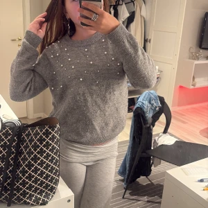 Grå stickad tröja med pärlor H&M - Supermysig grå stickad tröja från H&M med pärldetaljer framtill. Tröjan har rund halsringning, ribbade muddar och lång ärm. Perfekt för dig som gillar en enkel men ändå extra look med pärlor som sticker ut.