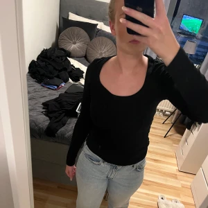 Svart ribbad långärmad tröja - Säljer en svart, ribbad långärmad tröja med rundad, djupare halsringning. Tröjan har en tight passform och är perfekt att styla med jeans eller kjol. Materialet är stretchigt och mjukt, vilket gör den riktigt skön att bära.