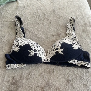Intimmissimi bh - Supersnygg mörkblå bh med krämvit blommig spets över kuporna och axelbanden. Justerbara band och klassisk knäppning bak. Den är väl använd med inga synliga tecken på användning. Köpt för 519 kr. Säljer då den är för liten💕