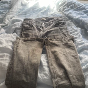 Young gina trico jeans  - Säljer ett par grå jeans med utsvängd passform och låg midja. Jeansen har klassisk femficksdesign och en silvrig stjärna på ena bakfickan som cool detalj. Materialet är mjukt denim och färgen är snyggt tvättad grå. Perfekta för dig som gillar en avslappnad men trendig look. Ps om du ser på bilden så har den lite slitna längst ner på byxorna 