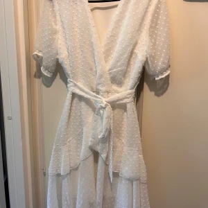Vit klänning strl S  - Vit omlott kort klänning i strl S. Avtagbart skärp i midjan. Material: 100% polyester. Mycket fint skick. 