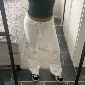Vita bootcut jeans med låg midja - Säljer ett par vita jeans med bootcut-modell och låg midja. Snygg passform som sitter tajt upptill och släpper vid benen. Klassisk femficksdesign och bälteshällor. Perfekta till sneakers eller boots för en fräsch look.
