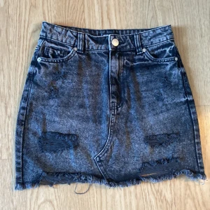 Svart jeanskjol från FB Sister storlek XS - Snygg svart jeanskjol från FB Sister i storlek XS. Kjolen har slitna detaljer, fransad nederkant och klassiska fickor både fram och bak. Perfekt för dig som gillar en edgy och trendig stil.