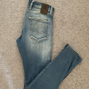 Replay Anbass ljusblå - Säljer ett par Replay Anbass jeans i ljusblå tvätt med slitningar och snyggt sliten look. Jeansen är i storlek W29 och L32. Skön tvätt både bak o fram med en slitning på vänster knä. Ett hål vid skrevet som är lappat ( se sista bilden)Enda  defekten! Hör av er vid funderingar!